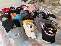 Photo of 25 assorted worn baseball caps and hats laid out on a bed including various colors and brands such as IZOD and Nautica. Used condition with signs of wear.