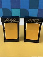 Two gold tone Zippo lighters in black display stands with Zippo branding visible.