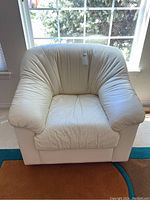 Front facing photo of a white leather armchair, showing the condition of the leather upholstery with visible creases and a plush cushion.