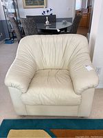 Front view of off-white leather armchair with creased leather upholstery and broad padded armrests.
