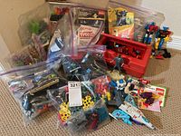 Overview of lot including various bags of LEGO pieces, a red box, Transformers toys, and assorted items scattered on the floor.