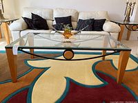 Front view of the glass top coffee table with wood legs and metal decorative accents, showing the clean glass surface and sturdy construction.