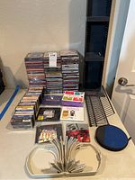 View of organized stacks of music CDs and tape cassettes with labels and accessories including CD holders and a soft case pouch on a table against a wall.