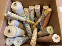 Top view showing multiple wallpaper rolls with varied patterns tightly rolled and arranged inside a box
