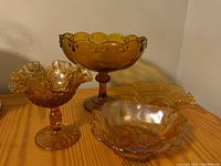 Four amber glass bowls of different shapes on wooden surface.