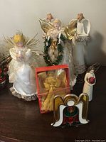 Seven angel figures including two lighted tree toppers, stained glass style candle holder, two tall composite tea light holders, and additional fabric angel figurines.
