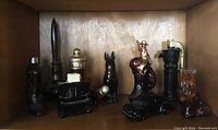 Photo showing nine vintage Avon glass perfume and cologne bottles arranged on a wooden shelf, featuring different shapes including a boot, piano, rider on horse, dog, nutcracker soldier, and others.