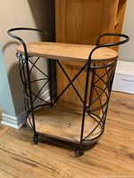 Bar cart shown fully from the front with the metal wire frame, top and bottom wood shelves, rounded ends on shelves, and visible casters on four legs.