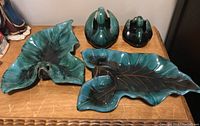 Four drip glaze Blue Mountain Pottery pieces on wood surface: two leaf-shaped dishes and two swan figurines in blue-green and brown tones.
