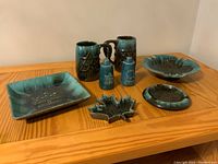 Overview of seven Blue Mountain Pottery items with green and brown glaze and 1867-1967 Centennial and Expo 67 star motif, arranged on wooden tabletop.
