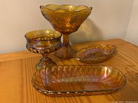 Set of four amber carnival glass pieces arranged on a wooden surface showing iridescent rainbow tones.