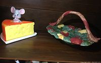 Photo shows the cheese cover shaped like a cheese wedge with mouse figurine beside the fruit-themed ceramic basket.