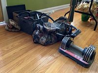 Photo shows a floral patterned gym bag, plastic basket with kettlebells, baseball glove and ball, and adjustable dumbbell on wood floor.
