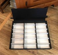 Open black eyeglass storage case showing 18 padded compartments for eyeglasses, arranged in three rows of six.