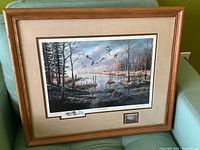 Framed print of wildlife scene with birds flying over water and trees, includes a small stamp and artwork signature.