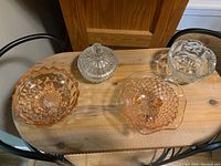 Lot displayed on wooden table showing four glass bowls: two clear including one covered, two pink footed bowls. Captures color, shape, details.