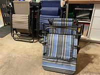 Three patio lounge chairs, two zero gravity chairs and one padded fabric folding lounge chair with blue and gray stripes, stacked and positioned in a garage.