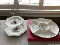 Two Nikko serving pieces displayed side by side, with the two-tiered serving dish on the left and sectioned serving dish on the right, showing holiday Christmas tree motifs and original box below sectioned dish.