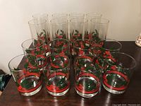 Photo showing eight tall glasses and eight tumblers arranged in two rows on a wooden surface, all with holly pattern print.