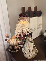 Photo showing four items: large Santa figure with yarn beard, Santa clamp lid jar, Santa candle holder, and wood HOHOHO sign in background.