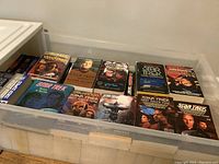 Photo showing the contents of a white storage box containing several Star Trek novels from various series including Deep Space Nine and The Next Generation.