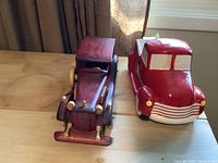 Wooden vintage car and red and white ceramic truck side by side on a wooden surface.