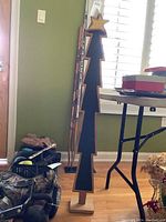 Wooden Christmas tree decoration standing on a wooden floor near a window with blinds and various household items around.