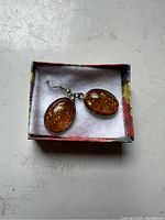 Pair of oval amber drop earrings in smooth silver-tone setting in a small lined box.