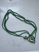 Three-stranded green jade bead necklace laid flat showing entire necklace with clasp visible.