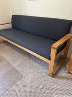 Wide angled side view showing the full vintage mid century modern couch with visible pine wood grain and dark upholstery, positioned on carpet.