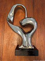 Front view of the metallic abstract sculpture on a wooden base showing smooth shiny curves and chrome finish.