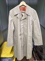 Front view of tan trenchcoat on hanger, showing buttoned collar and hidden front button placket.