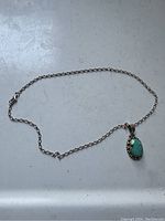 Full view of the sterling silver chain and turquoise stone pendant necklace laid flat