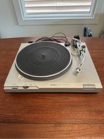 Full view of Technics SL-D1 direct drive turntable showing silver metal body, black rubber platter mat, tonearm, and wires on a wooden surface.