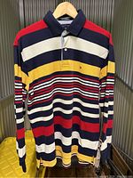 Front view of vintage Tommy Hilfiger striped long sleeve polo shirt showing multicolored horizontal stripes, collar, button placket, and logo embroidery.