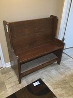 Front view of solid wood bench placed against a wall showing seating surface and lower shelf.