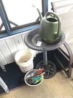 Full view of the outdoor items including the bird bath, watering jug, bucket, garden tools in stainless bowl, and adjacent chair.
