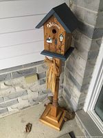Front and side views of the solid wood bird house on pedestal with painted decorative front and 'Welcome' text, tied with a raffia bow on the pedestal.