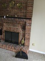 Photo of fireplace with black metal bellows, black metal log tray at hearth, small brass candle, and other brass items on mantle