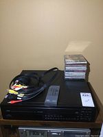 Front and top view of Yamaha CDC-715 CD player with remote control and RCA cables on top, several CDs stacked beside it.