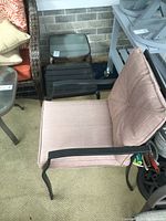 Outdoor metal chair with pinkish cushions sitting on floor by wall indoors with shelves and other furniture around