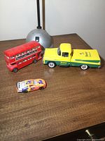 Die cast Beaver Lumber pickup truck bank, red double decker bus, and Tide Nascar car on wooden surface.
