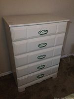 Front view of white dresser showing five drawers with green handles and panel detailing.