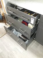 Three open kitchen drawers showing cutlery, storage containers, and bakeware with some utensils and appliances inside