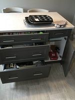 Overview of island showing multiple open drawers filled with miscellaneous kitchen utensils, and bakeware including muffin pans and baking sheets on counter above.