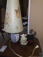 Full lot photo showing the lamp with floral shade, ceramic angel candle holder, and small desk organizer with magnifying glass on a wooden table.