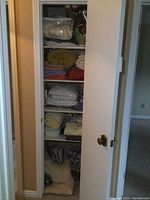 Photo of a white closet with sliding doors displaying stacked linens including blankets, towels, sheets, and knit sweaters.