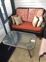 Plastic wicker loveseat with cushions and rectangular glass coffee table on indoor porch