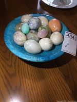 Top view showing the blue pedestal dish and the assortment of polished marble eggs of various sizes and colors inside it.