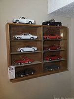 Full view of the wooden display case mounted on a wall with glass sliding doors visible, showing all 10 model cars displayed inside across two columns with five shelves each.